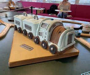 Left: A pool table covered in wooden train tracks and other toys, including a model crane from Tren holding a playing card. Right Top: A ping pong table, also heavily decorated. Right Bottom: A Tren cake!