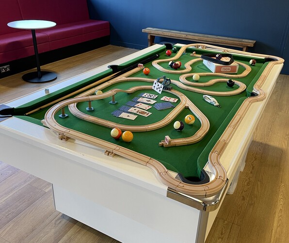 Left: A pool table covered in wooden train tracks and other toys, including a model crane from Tren holding a playing card. Right Top: A ping pong table, also heavily decorated. Right Bottom: A Tren cake!